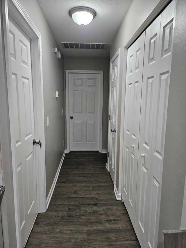 corridor with a textured ceiling and dark hardwood / wood-style floors