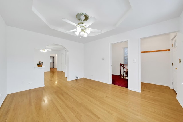 empty room with ceiling fan, light wood-type flooring, and a raised ceiling