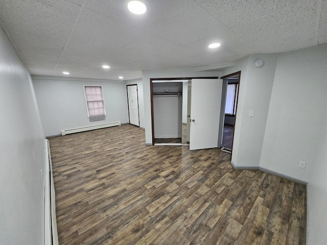 interior space with a drop ceiling, a baseboard heating unit, and dark hardwood / wood-style flooring