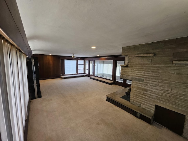 unfurnished living room featuring a fireplace, light colored carpet, and wooden walls