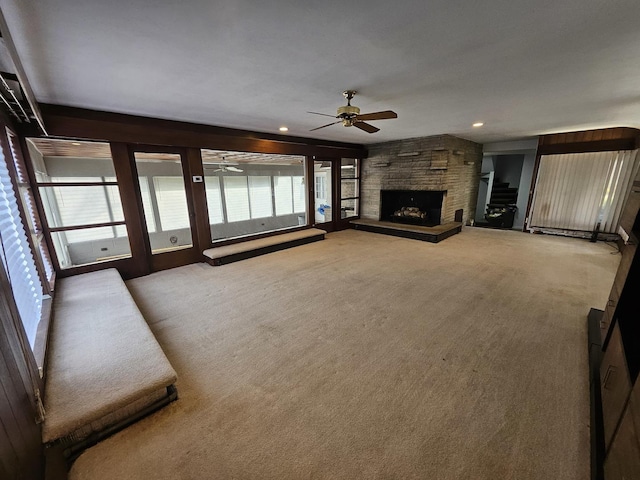 unfurnished living room with ceiling fan, a stone fireplace, and carpet