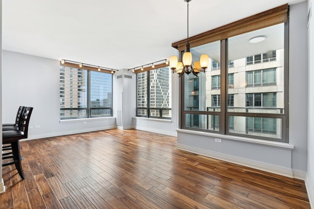 unfurnished dining area with track lighting, an inviting chandelier, and dark hardwood / wood-style floors