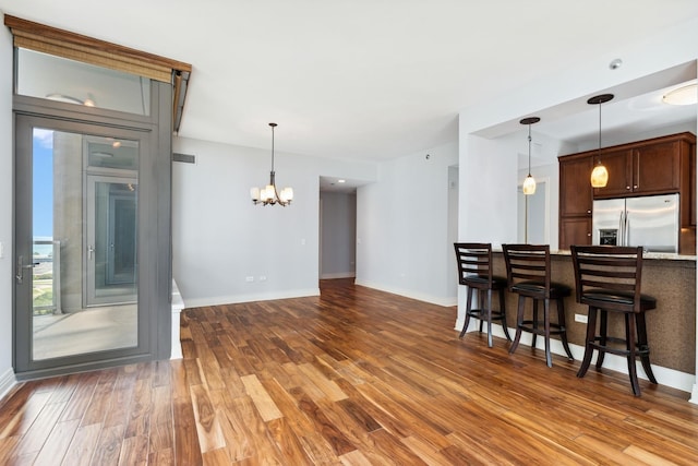 kitchen featuring a chandelier, stainless steel refrigerator with ice dispenser, a breakfast bar area, wood-type flooring, and dark brown cabinetry