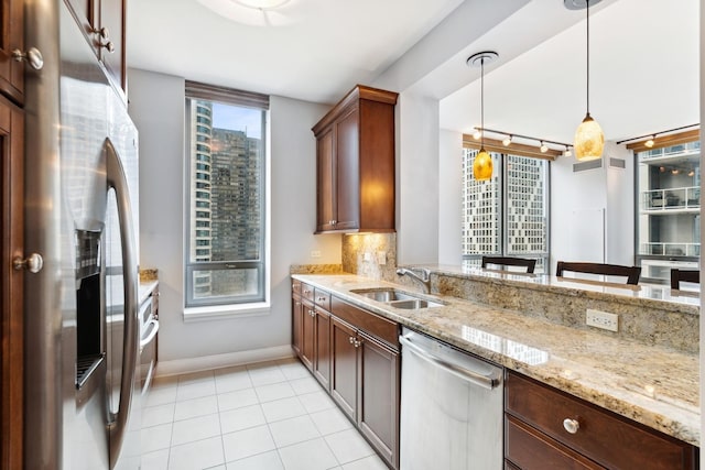 kitchen featuring light stone counters, decorative light fixtures, backsplash, appliances with stainless steel finishes, and sink