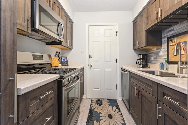 kitchen with appliances with stainless steel finishes, dark brown cabinets, a textured ceiling, light hardwood / wood-style flooring, and sink