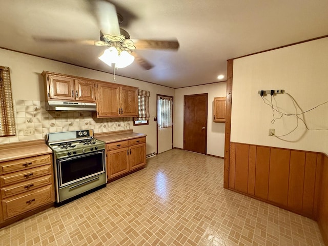 kitchen featuring wood walls, ceiling fan, gas range, and tasteful backsplash