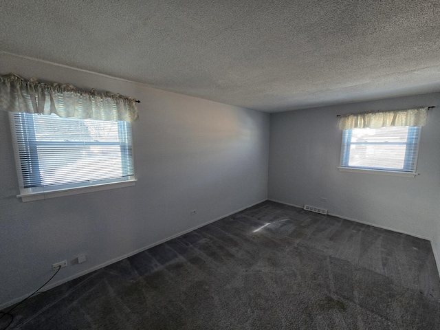 spare room featuring a textured ceiling and dark carpet