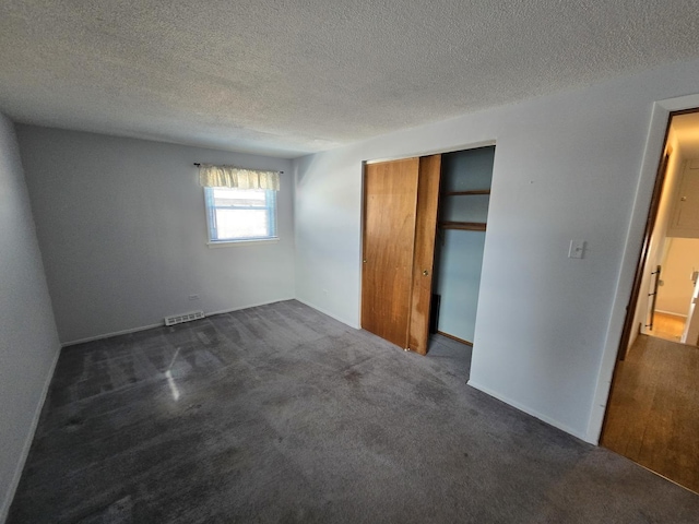 unfurnished bedroom with dark carpet, a closet, and a textured ceiling