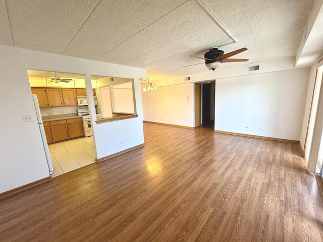 unfurnished living room with a textured ceiling, light wood-type flooring, and ceiling fan with notable chandelier