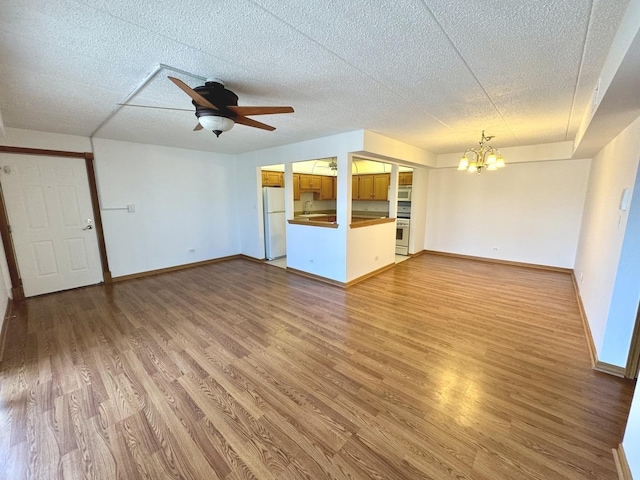 unfurnished living room with ceiling fan with notable chandelier, sink, and hardwood / wood-style floors