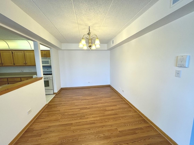 unfurnished dining area featuring a textured ceiling, a chandelier, and hardwood / wood-style floors