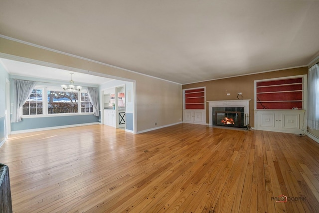 unfurnished living room featuring light wood-type flooring, built in features, crown molding, and an inviting chandelier