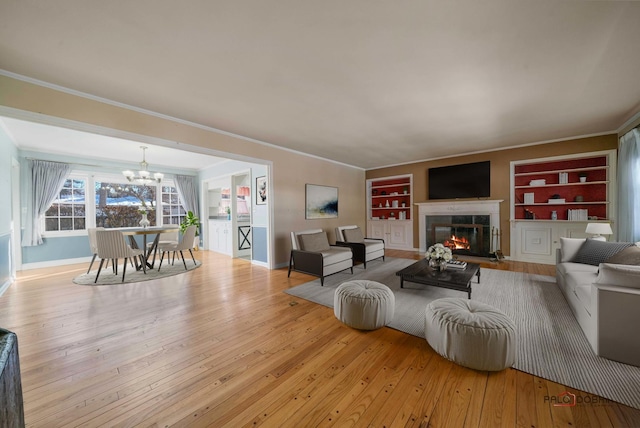 living room featuring an inviting chandelier, crown molding, light hardwood / wood-style floors, and built in features