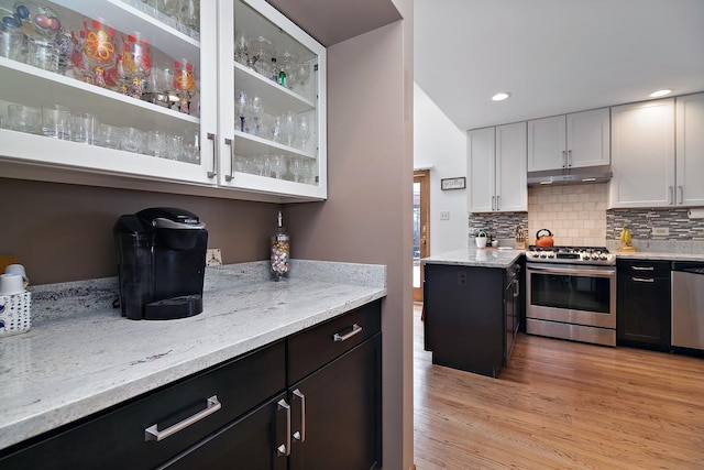 kitchen featuring tasteful backsplash, white cabinets, stainless steel appliances, light stone countertops, and light wood-type flooring