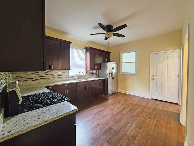 kitchen with gas stove, hardwood / wood-style floors, backsplash, light stone countertops, and stainless steel refrigerator with ice dispenser