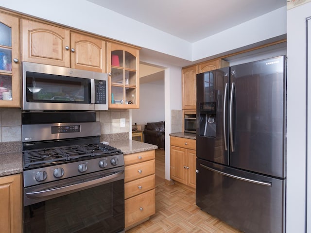 kitchen featuring stainless steel appliances, light parquet flooring, dark stone countertops, and tasteful backsplash