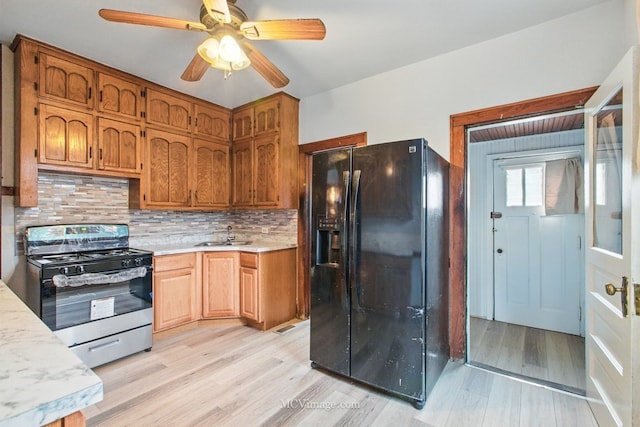 kitchen featuring gas range oven, black refrigerator with ice dispenser, light wood-style floors, and light countertops
