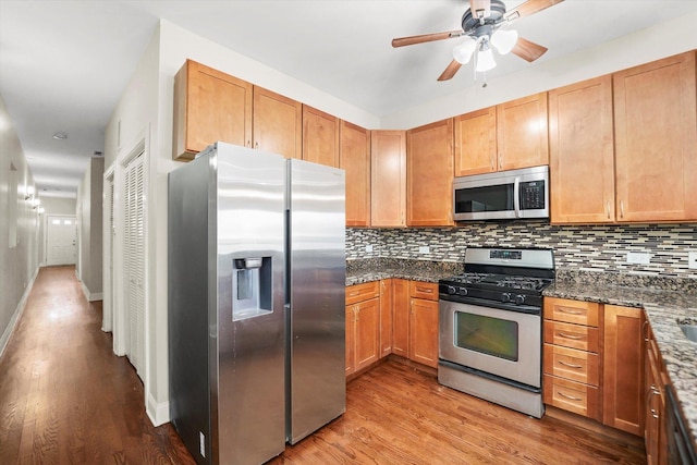 kitchen featuring appliances with stainless steel finishes, tasteful backsplash, dark stone counters, ceiling fan, and light hardwood / wood-style floors