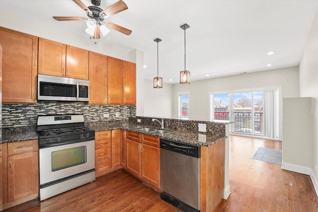 kitchen with sink, hanging light fixtures, dark stone counters, kitchen peninsula, and stainless steel appliances