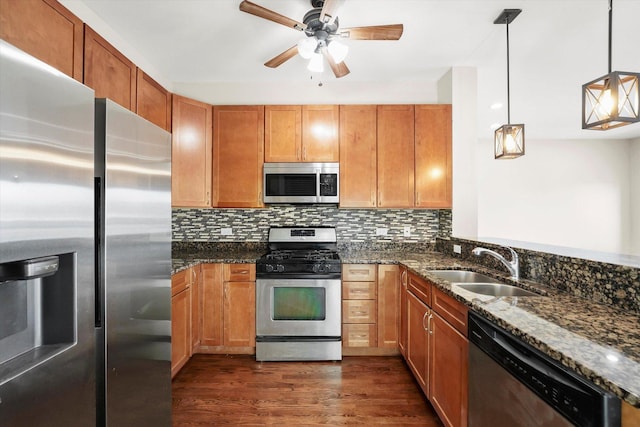 kitchen with stainless steel appliances, sink, dark stone countertops, and decorative light fixtures