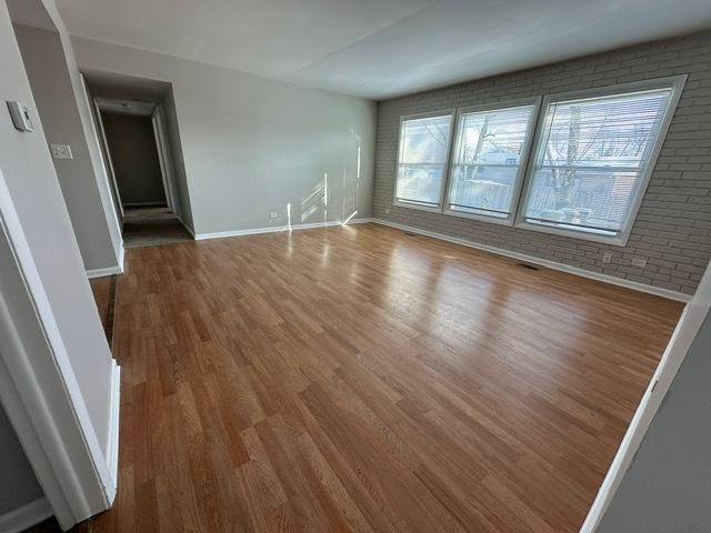 unfurnished room with brick wall and hardwood / wood-style floors