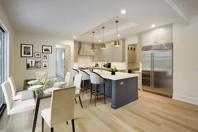 kitchen with a raised ceiling, custom range hood, appliances with stainless steel finishes, a breakfast bar area, and light wood-type flooring