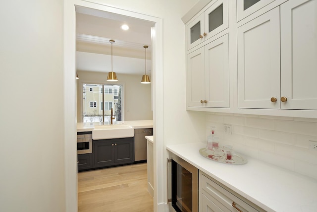 bar with light wood-style flooring, beverage cooler, a sink, hanging light fixtures, and tasteful backsplash