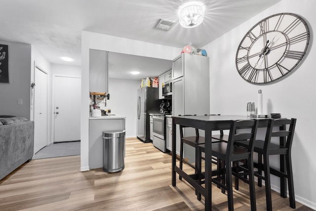 kitchen with appliances with stainless steel finishes, gray cabinetry, and light wood-type flooring