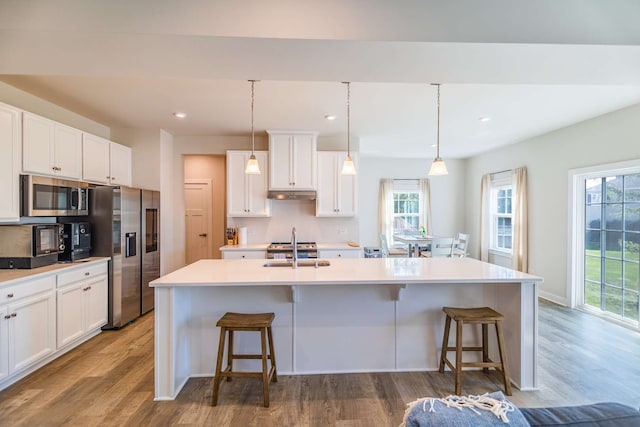 kitchen featuring a center island with sink, stainless steel appliances, hanging light fixtures, a kitchen bar, and sink