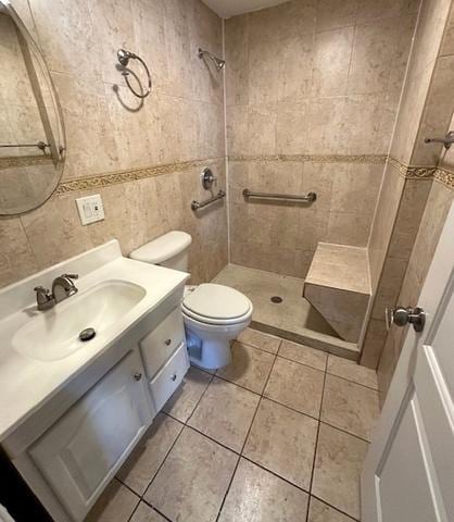 bathroom featuring tile patterned flooring, toilet, vanity, tile walls, and a tile shower