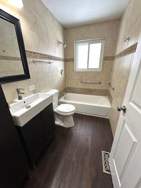 full bathroom featuring tiled shower / bath, tile walls, hardwood / wood-style floors, toilet, and vanity