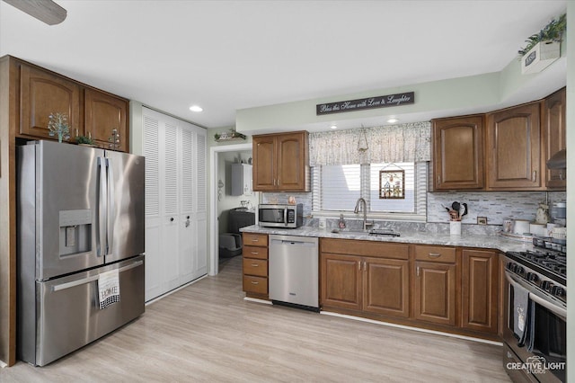 kitchen with light stone counters, stainless steel appliances, tasteful backsplash, light wood-type flooring, and sink