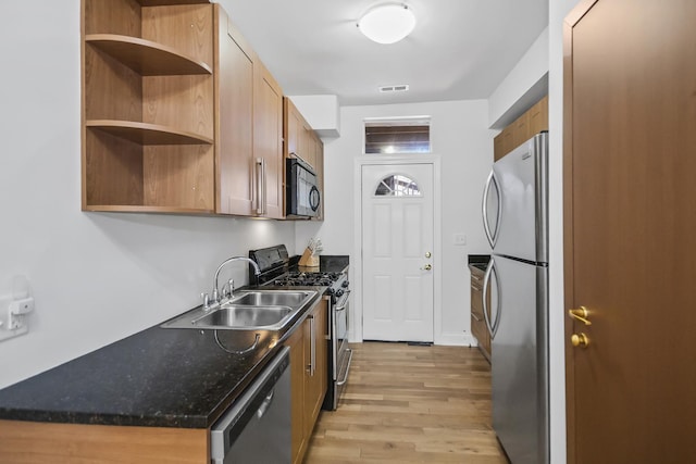 kitchen featuring sink, light wood-type flooring, dark stone counters, and appliances with stainless steel finishes