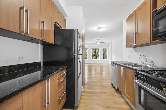 kitchen with sink, ceiling fan, light hardwood / wood-style flooring, dark stone counters, and appliances with stainless steel finishes