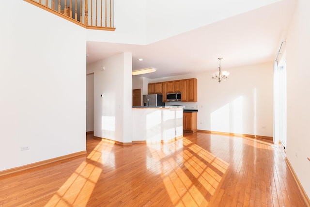 unfurnished living room with a high ceiling, an inviting chandelier, and light hardwood / wood-style flooring