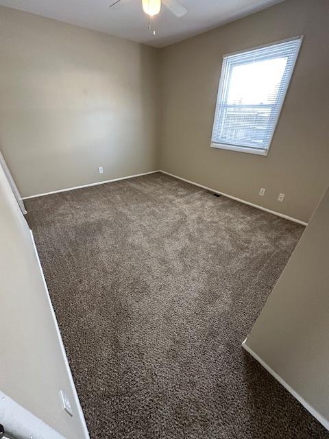 spare room featuring ceiling fan and dark colored carpet