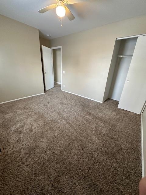 unfurnished bedroom with ceiling fan, a closet, and dark colored carpet