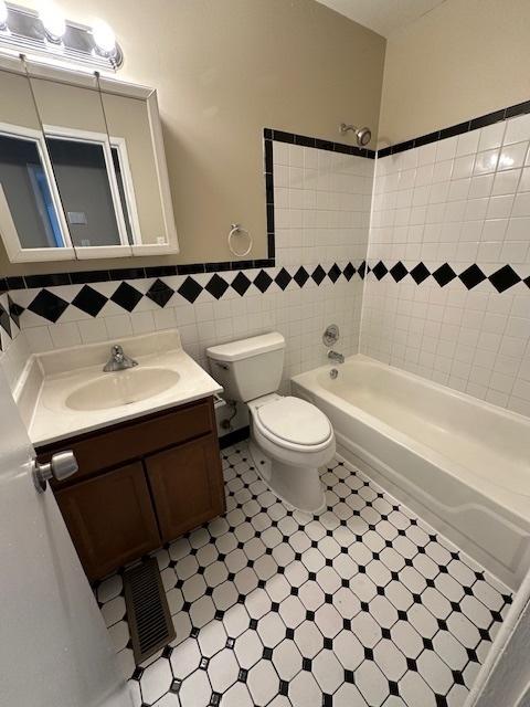 full bathroom with tile walls, vanity, tiled shower / bath combo, and toilet