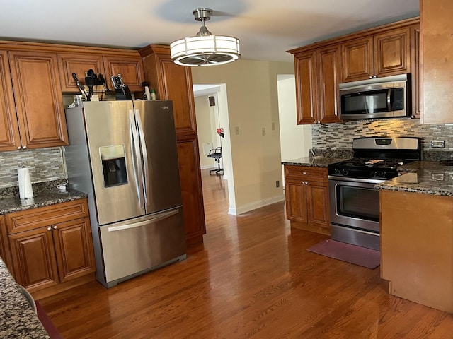 kitchen featuring tasteful backsplash, appliances with stainless steel finishes, decorative light fixtures, and dark stone countertops