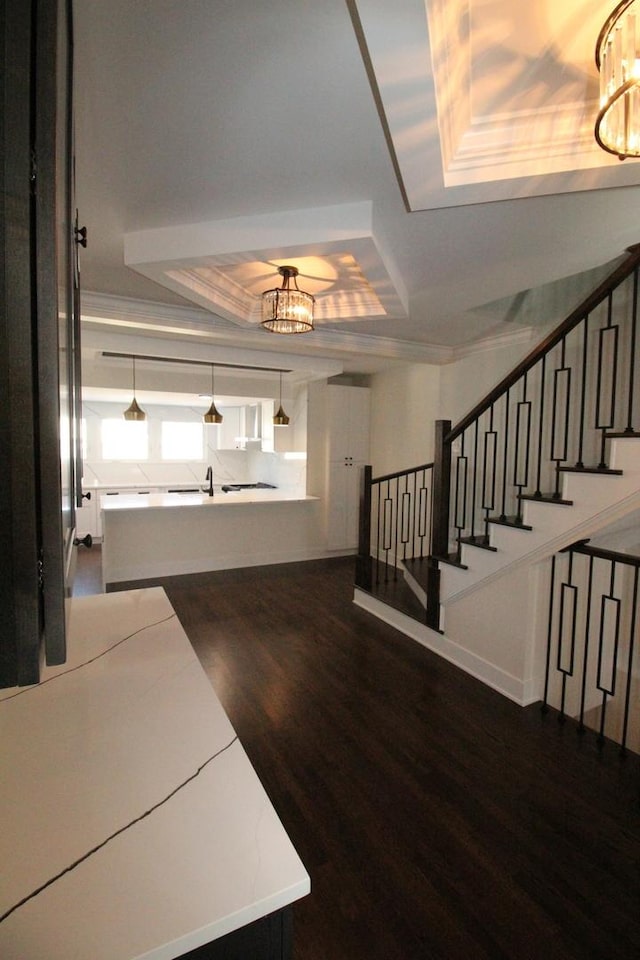 entrance foyer featuring a raised ceiling, a chandelier, dark hardwood / wood-style flooring, and ornamental molding