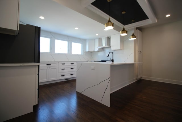 kitchen with dark hardwood / wood-style floors, wall chimney range hood, pendant lighting, decorative backsplash, and white cabinets