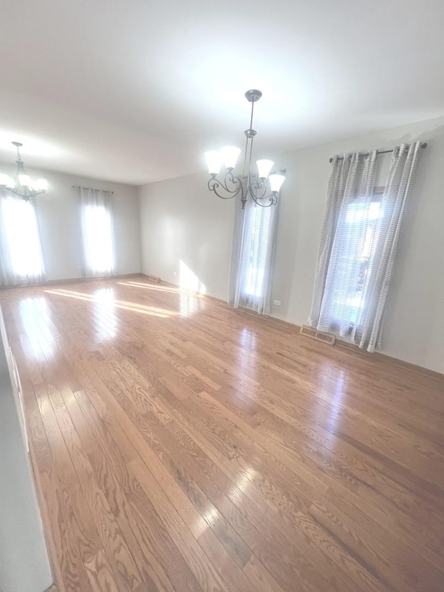 spare room with an inviting chandelier and hardwood / wood-style flooring