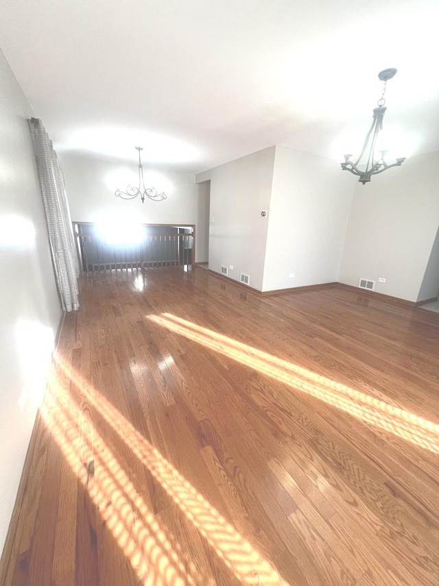 spare room with an inviting chandelier and hardwood / wood-style floors