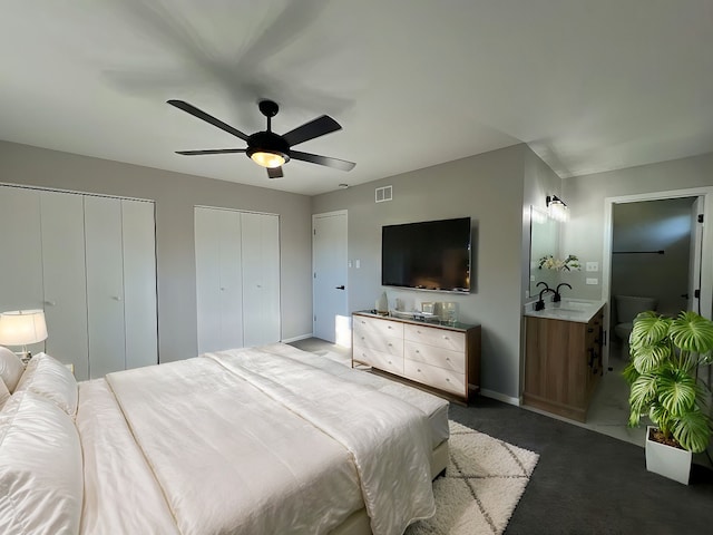 carpeted bedroom with two closets, ceiling fan, and sink