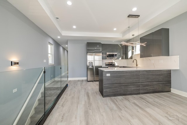 kitchen featuring kitchen peninsula, pendant lighting, stainless steel appliances, light wood-type flooring, and a tray ceiling