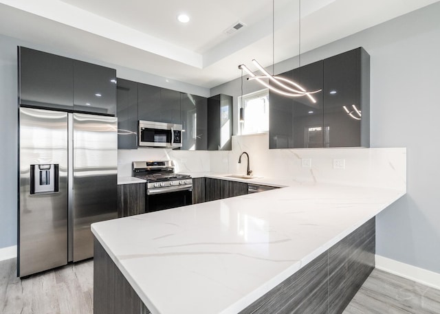 kitchen featuring kitchen peninsula, light stone countertops, hanging light fixtures, stainless steel appliances, and sink