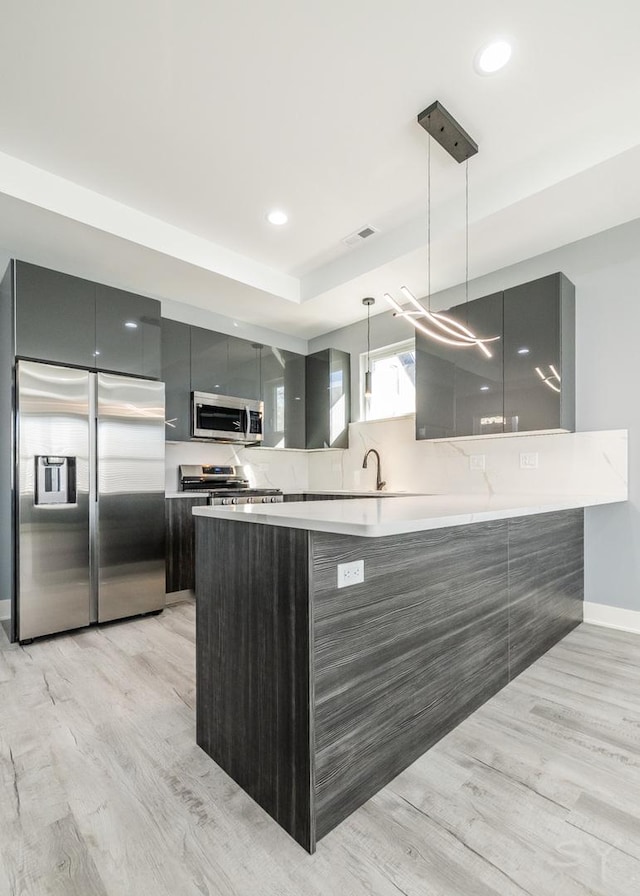 kitchen featuring gray cabinets, stainless steel appliances, kitchen peninsula, pendant lighting, and light hardwood / wood-style flooring