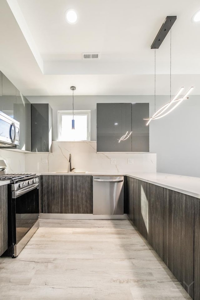 kitchen featuring stainless steel appliances, decorative light fixtures, sink, and dark brown cabinets