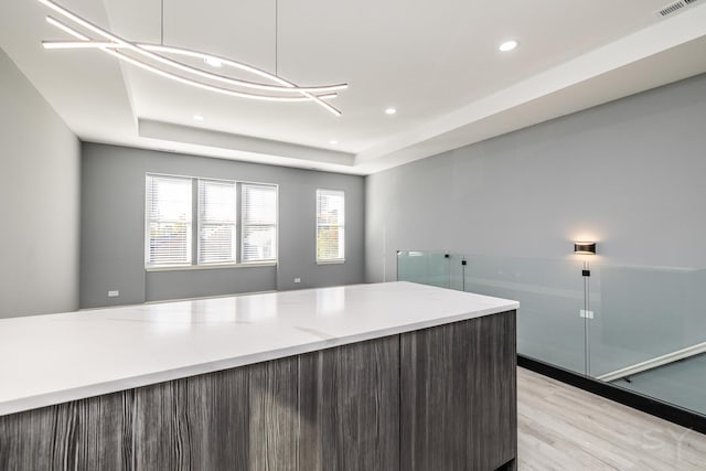 kitchen with light hardwood / wood-style floors, pendant lighting, a tray ceiling, and light stone counters