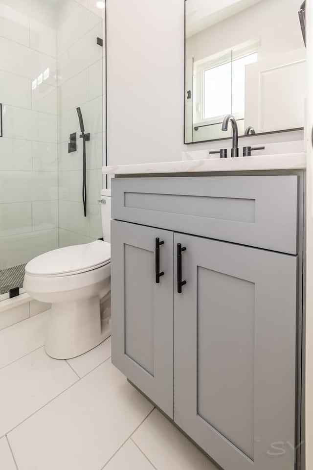 bathroom with toilet, tile patterned floors, tiled shower, and vanity